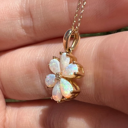 10k gold opal and diamond flower necklace on gold chain shown close-up in hand under sunlight