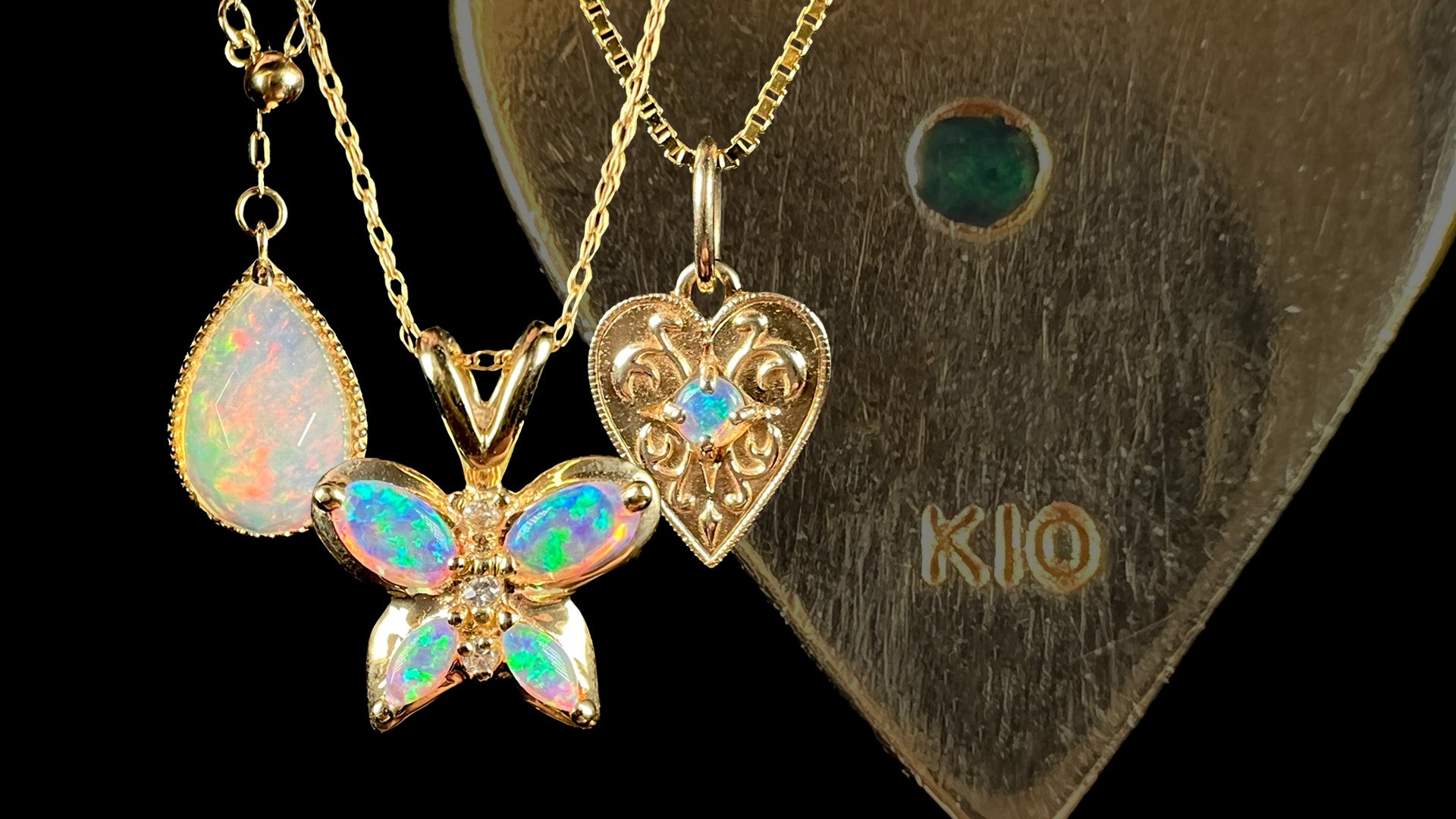 Three 10k gold opal necklaces including pear shape, butterfly, and heart design in front of faded gold opal pendant with "K10" hallmark stamp in focus.