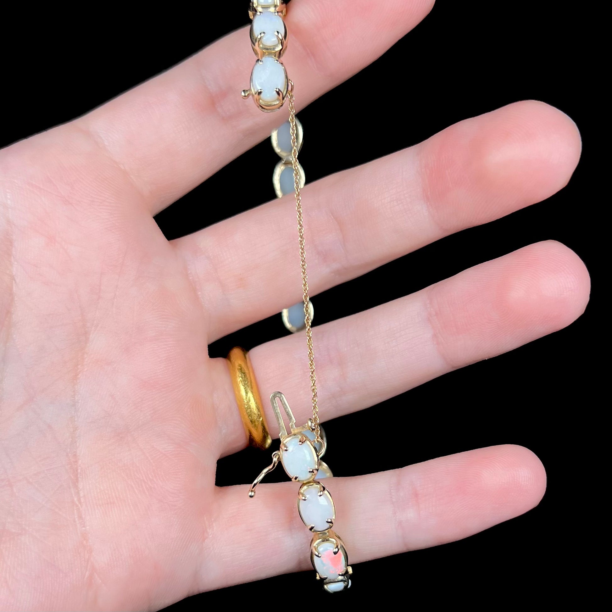 Hand holding white opal bracelet open, showing the length of its 10k yellow gold safety chain and box clasp.
