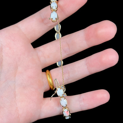 Hand holding white opal bracelet open, showing the length of its 10k yellow gold safety chain and box clasp.