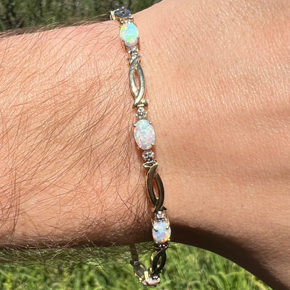 Close-up of 10k yellow gold lab-created opal and diamond chip tennis bracelet worn on wrist in natural light.