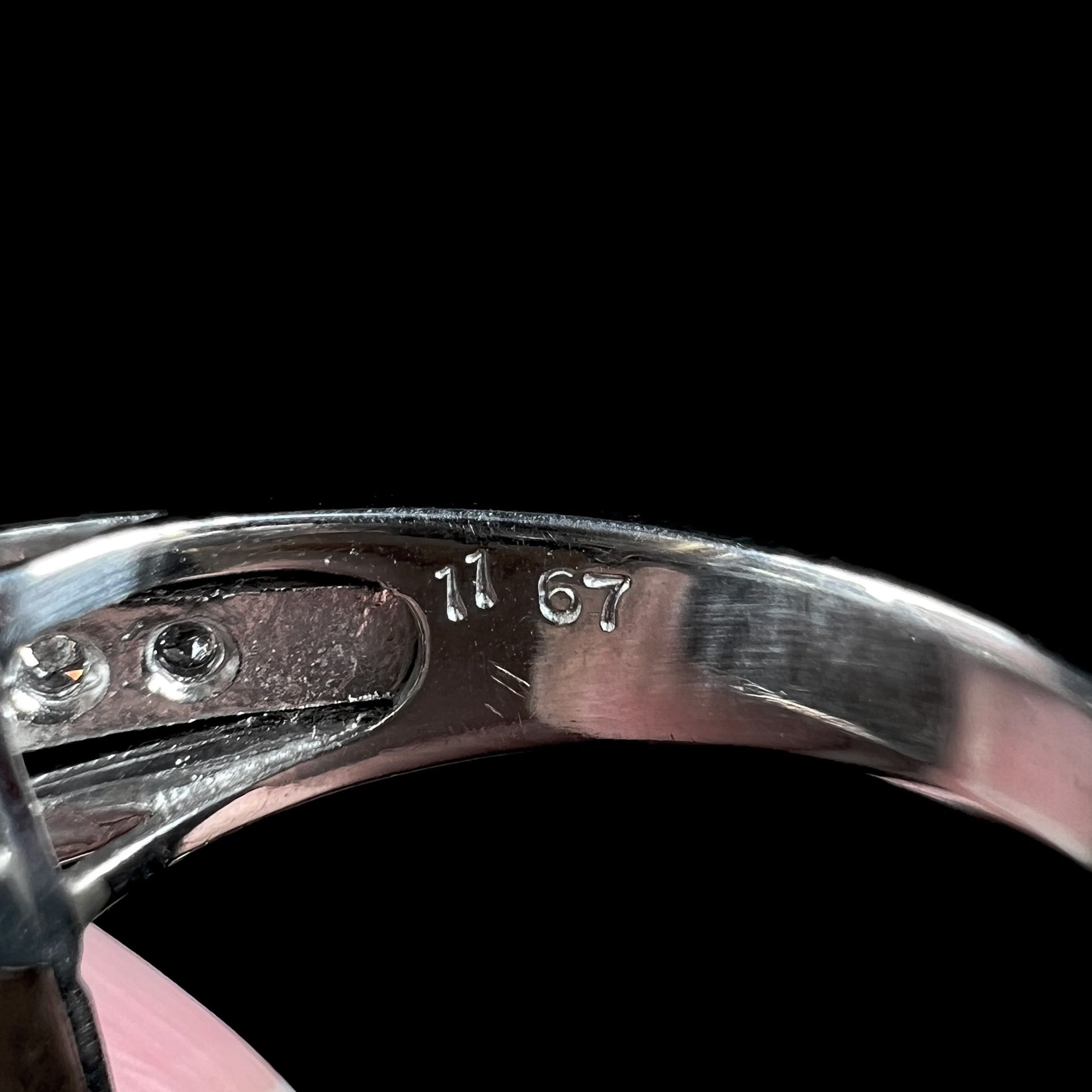 Inside of a diamond-accented platinum ring's shank showing the hallmark, "11 67".