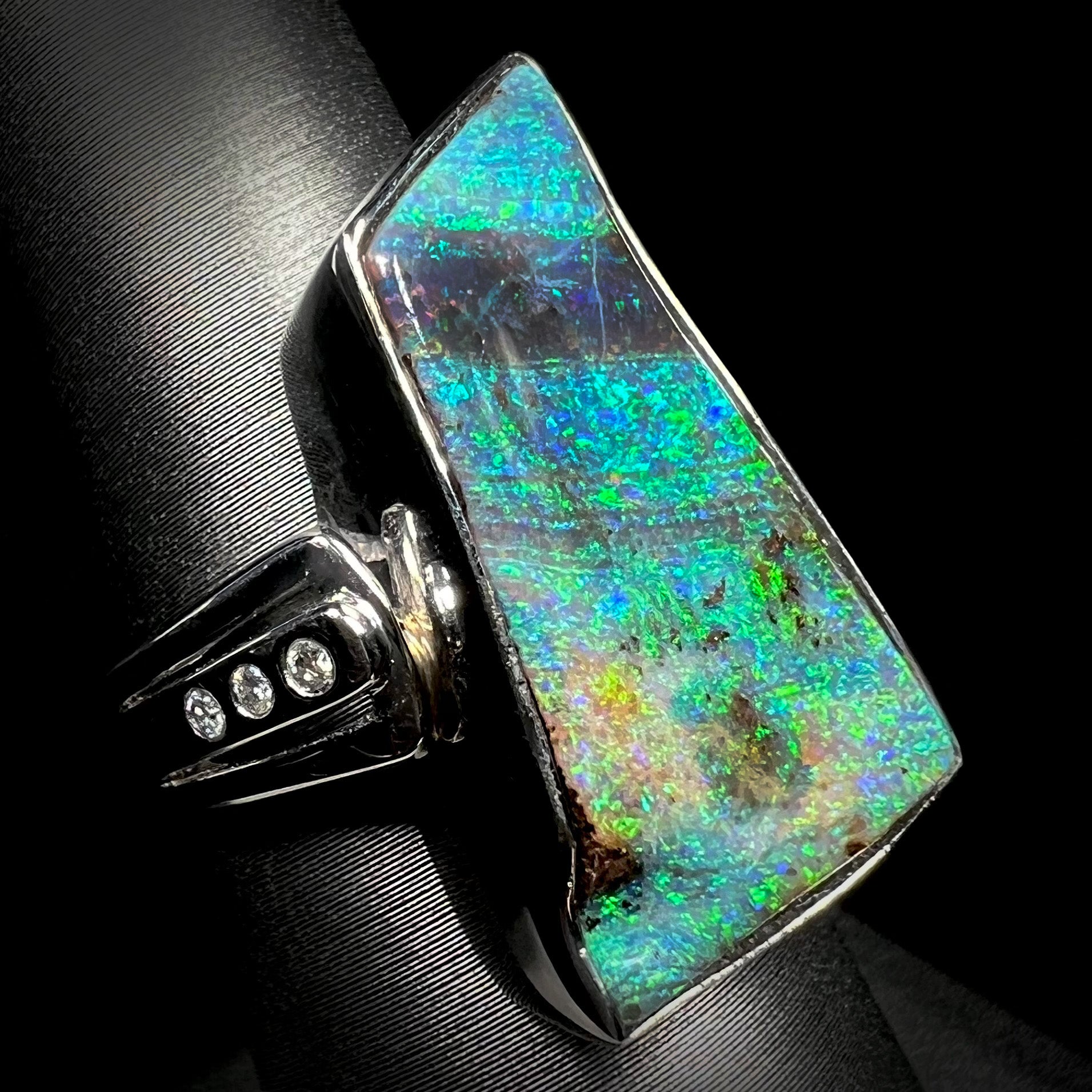 An 11.67ct Australian boulder opal and diamond ring in platinum, shown on a ring display at an angled view.