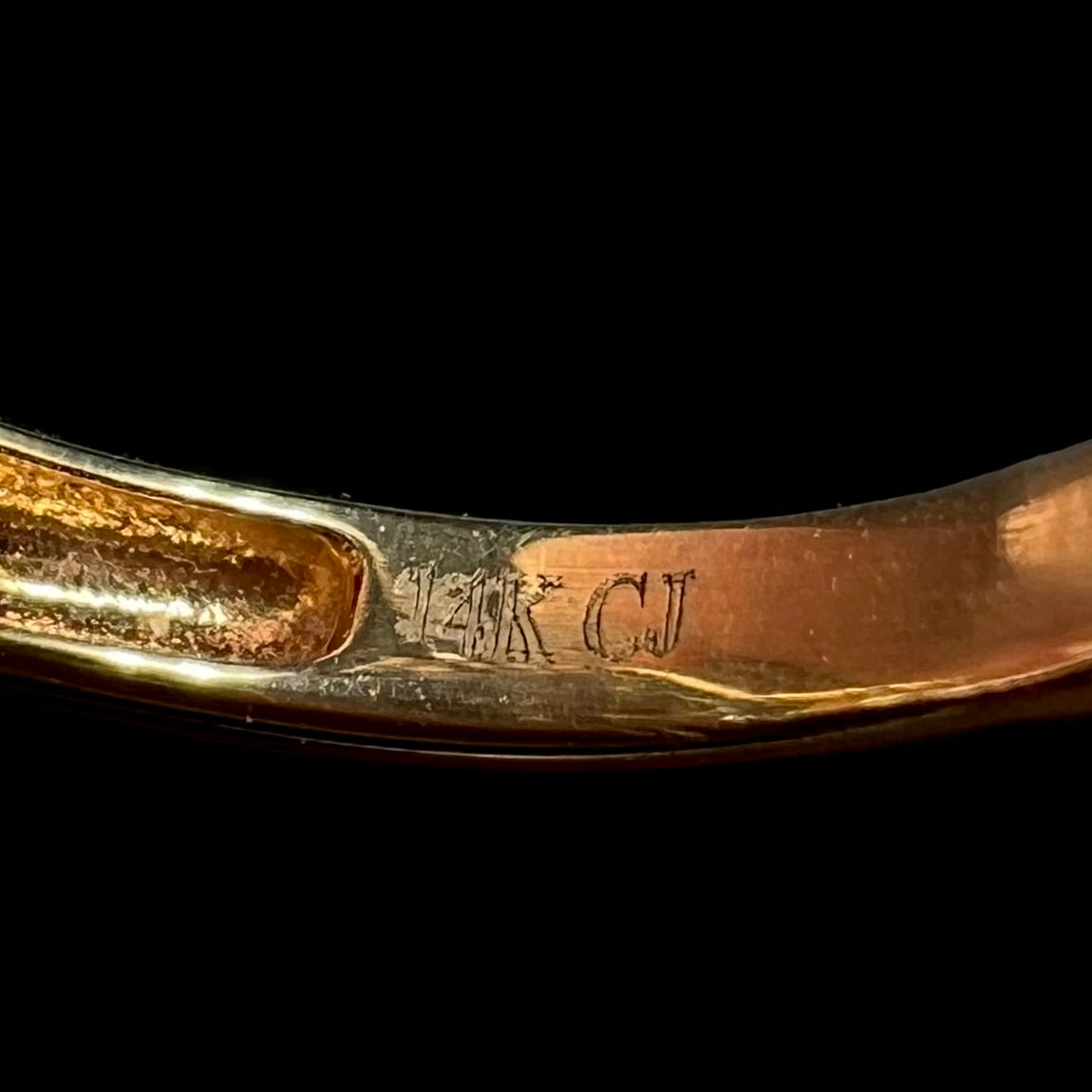 Close-up of the inside of a gold ring's shank, showing the laser-etched hallmark stamps "14K" and "CJ", denoting designer Cirari Jewels.