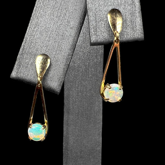 Front view of 14k gold round Australian opal drop earring pair shown on earring display against black background.  One opal is greenish blue, the other is orange.