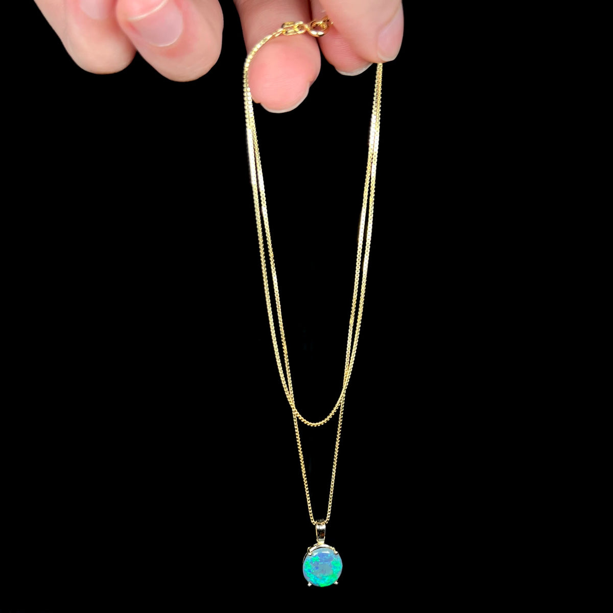 Fingers dangling a gold-tone necklace from chain with dainty 14k gold black opal women's pendant