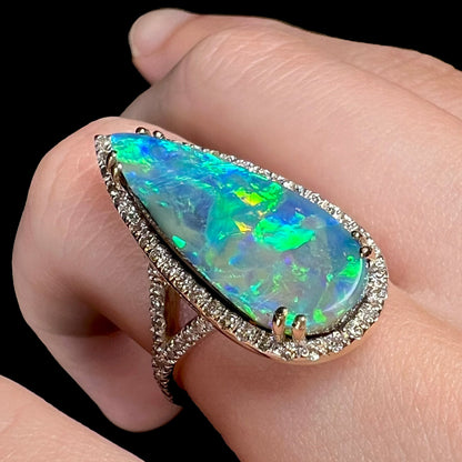 A 14k yellow gold boulder opal ring with a VS2 diamond-accented halo shown close-up from an angle, worn on a finger.
