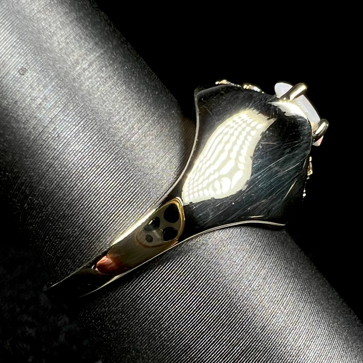 A 14k yellow gold domed ring prong-set with an opal, shown from the side view on ring display; the ring's shank is primarily in focus, the sides of the opal barely visible