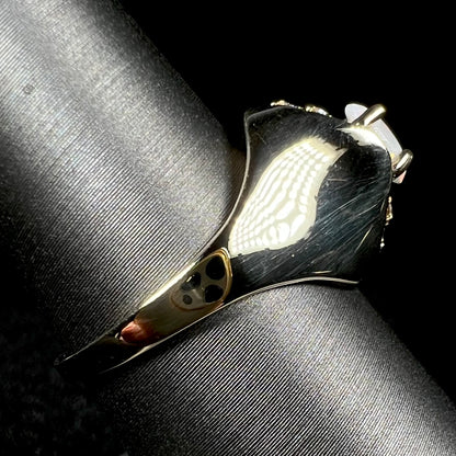 A 14k yellow gold domed ring prong-set with an opal, shown from the side view on ring display; the ring's shank is primarily in focus, the sides of the opal barely visible