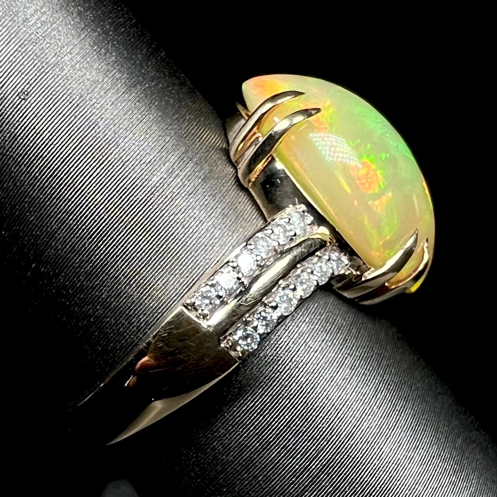 Side view of 14k yellow gold Ethiopian opal and diamond pave ring with split prong design, shown on display, focused on ring's shank