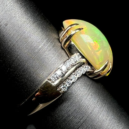 Side view of 14k yellow gold Ethiopian opal and diamond pave ring with split prong design, shown on display, focused on ring's shank