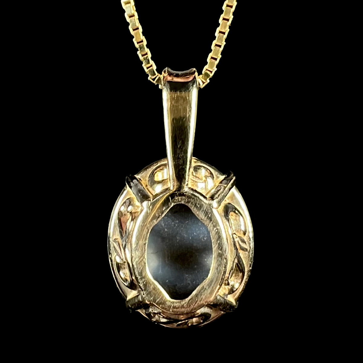 Back side of 14k yellow gold filigree basket pendant set with black opal; the black opal's natural potch backing visible