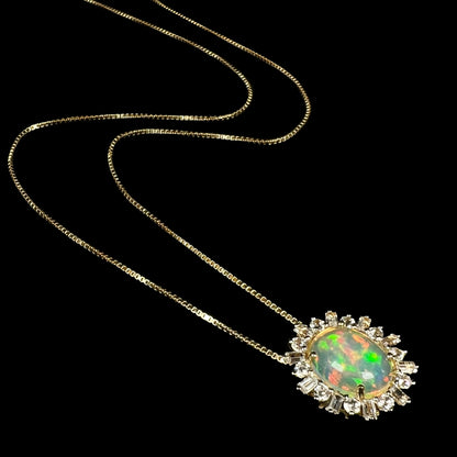 Angled view of 14k yellow gold fire opal and white sapphire halo necklace shown laying on black background.