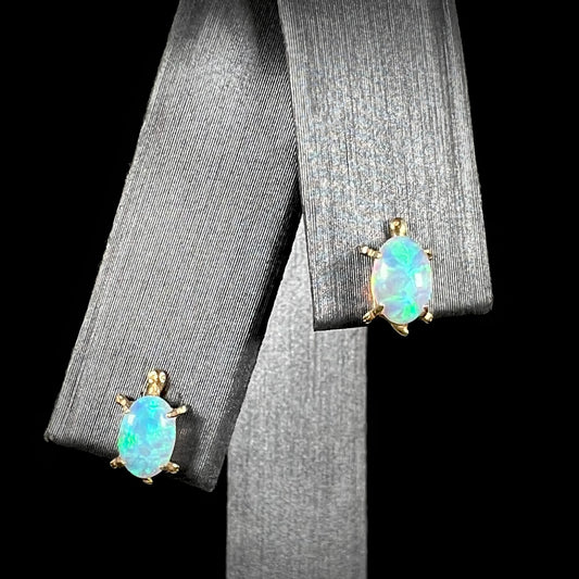 A close-up front view of 14k gold lab-created opal turtle stud earrings, featuring vibrant blue and green opal fire, displayed against a black background.