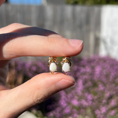 A macro close-up of 14k gold opal and diamond clip-on earrings in natural sunlight, revealing vibrant green and red opal fire against a gold setting.