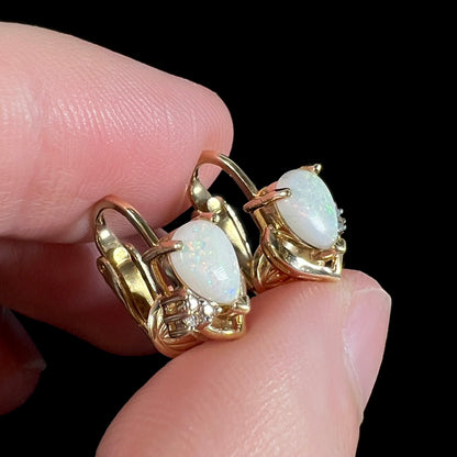 A detailed macro view of 14k gold opal and diamond clip-on earrings held at an alternate angle, showcasing their elegant gold setting and natural opals.