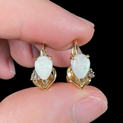 A macro close-up of 14k gold opal and diamond clip-on earrings held in fingers, capturing their natural opal fire with subtle reddish color play.