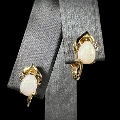 A close-up front view of 14k gold opal and diamond clip-on earrings, featuring natural white opals and diamond accents, displayed on a black background.