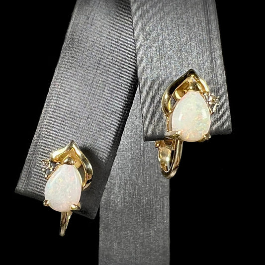 A close-up front view of 14k gold opal and diamond clip-on earrings, featuring natural white opals and diamond accents, displayed on a black background.