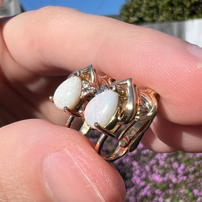 An angled macro view of 14k gold opal and diamond clip-on earrings in natural sunlight, showing faint, subtle red opal flashes against the gold setting.