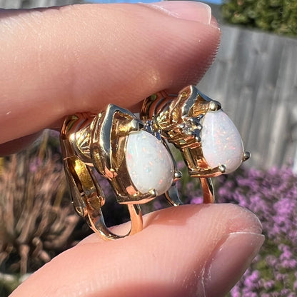 A close-up macro shot of 14k gold opal and diamond clip-on earrings in natural light, held at an alternate angle to display subtle opal color play.