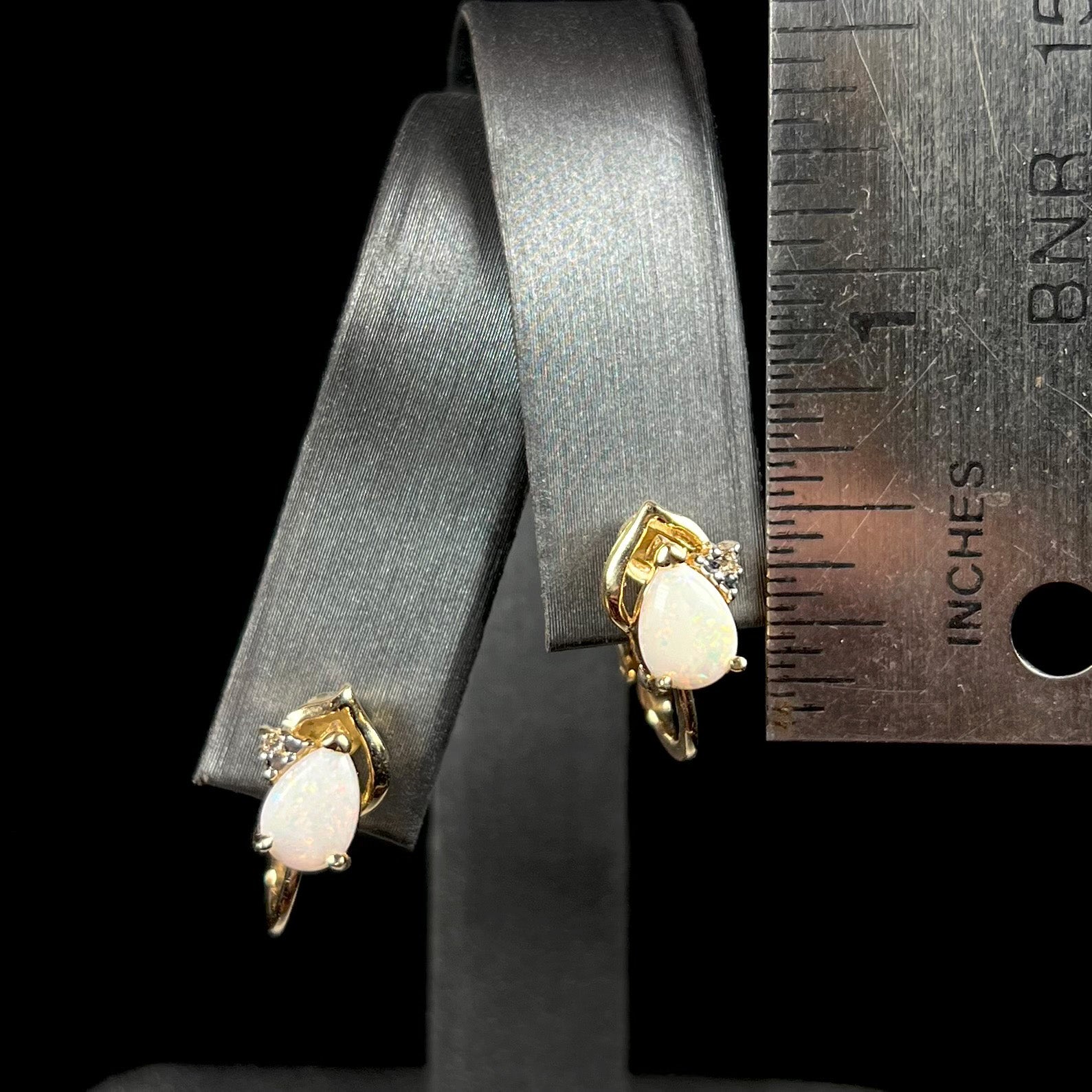 A pair of 14k gold opal and diamond clip-on earrings next to a ruler, showing their petite 0.66 inch size for scale.