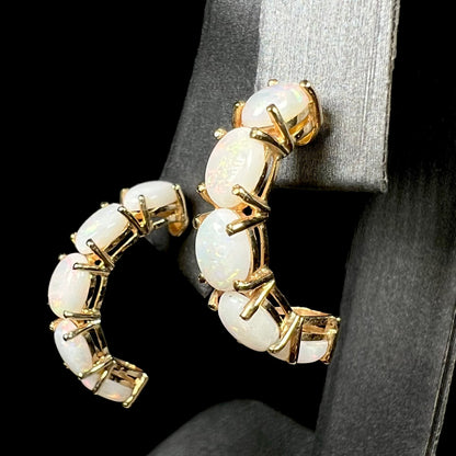 Angled close-up of vintage c.1990s 14k gold Australian opal semi-hoop earrings on earring display; the opals are held by prongs