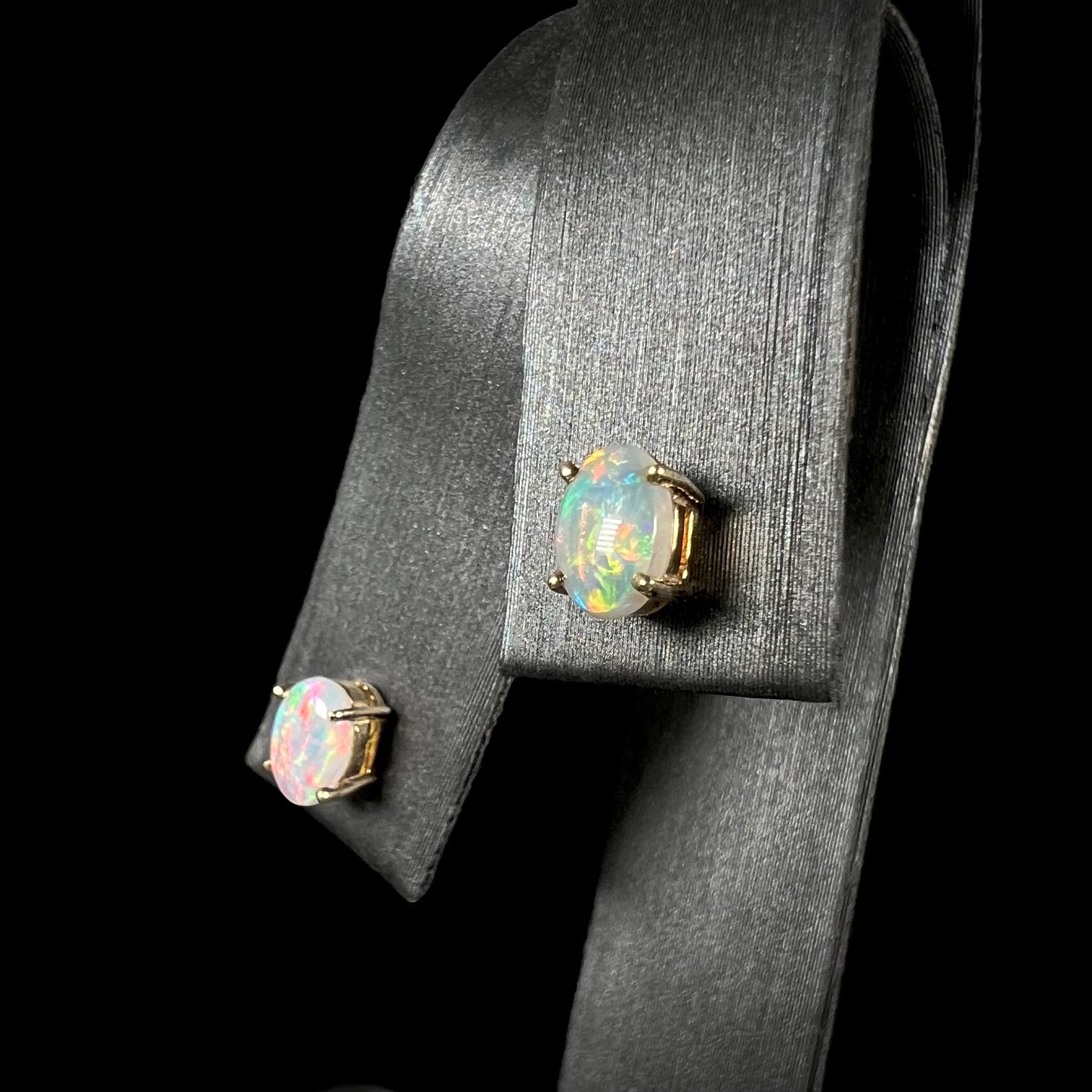 An angled view of 14k gold opal stud earrings, one opal showing pink tones and the other displaying blue and orange.