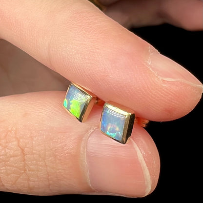 14k gold opal earrings with square shape held in fingers.  One opal has a green flash