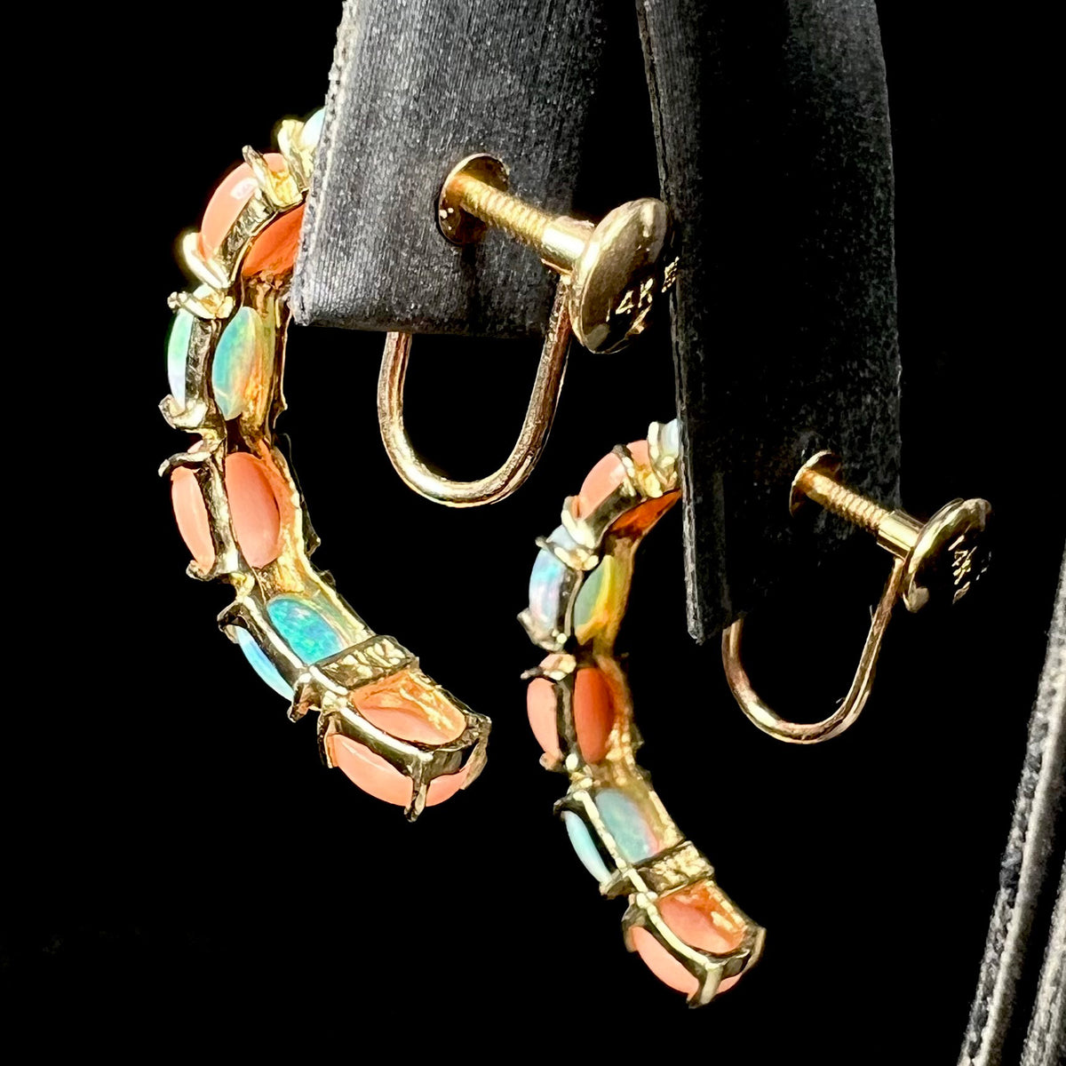 Back side of opal and coral semi-hoop earrings on earring display, their 14k gold non-pierced screw backs in focus