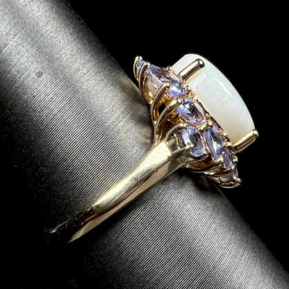 A 14k yellow gold white opal and tanzanite-accented ring shown on a ring display from the side view, the ring's polished shank in focus
