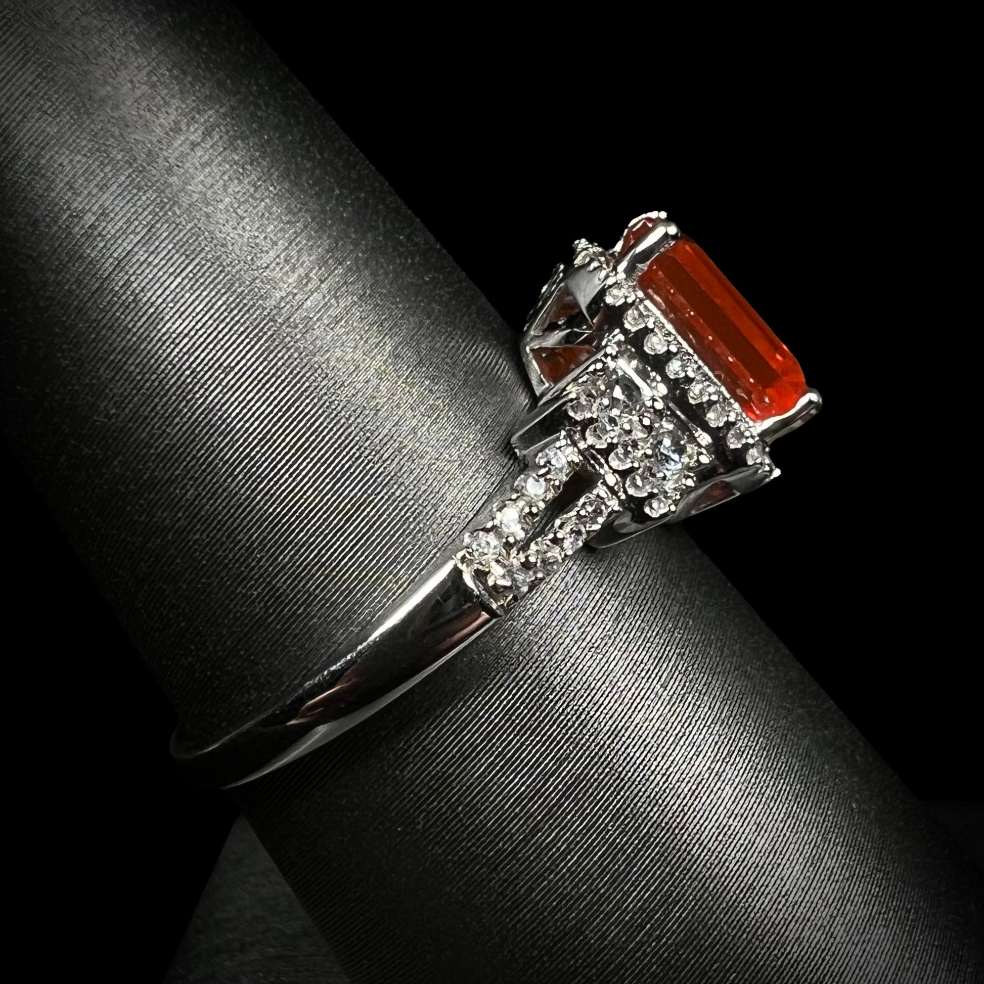 Side view of a 14k white gold fire opal and white zircon ring focusing on the ring's split shank design, shown on a ring display against a black backdrop.