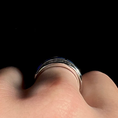 Side profile gallery view of a 14k white gold ring, worn on a hand; the blue opal inlay is flush along the ring's surface, barely in view
