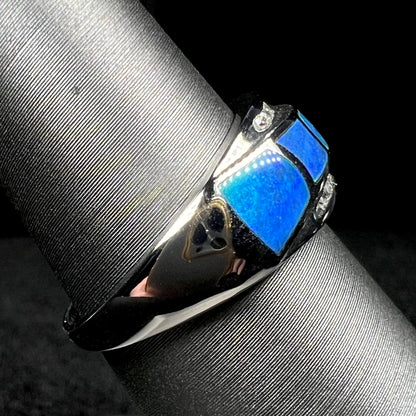 A 14k white gold opal inlay ring shown on ring display from side view, its shank and blue opal side inlay in focus