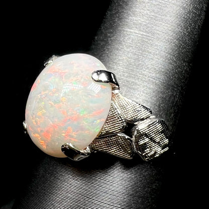 Angled close-up of a 14k white gold natural opal ring with a textured shoulder design, shown on ring display
