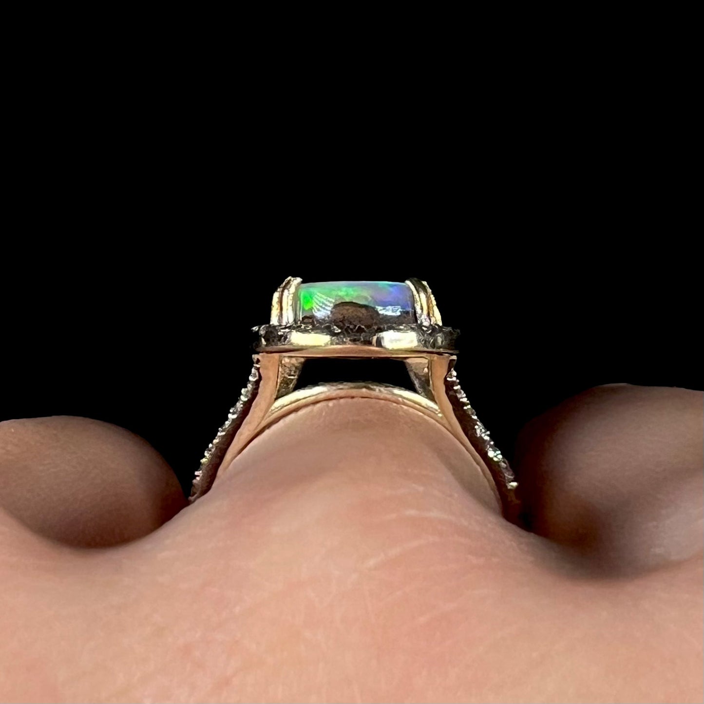Gallery profile view of a 14k yellow gold boulder opal ring worn on a finger against a black backdrop.