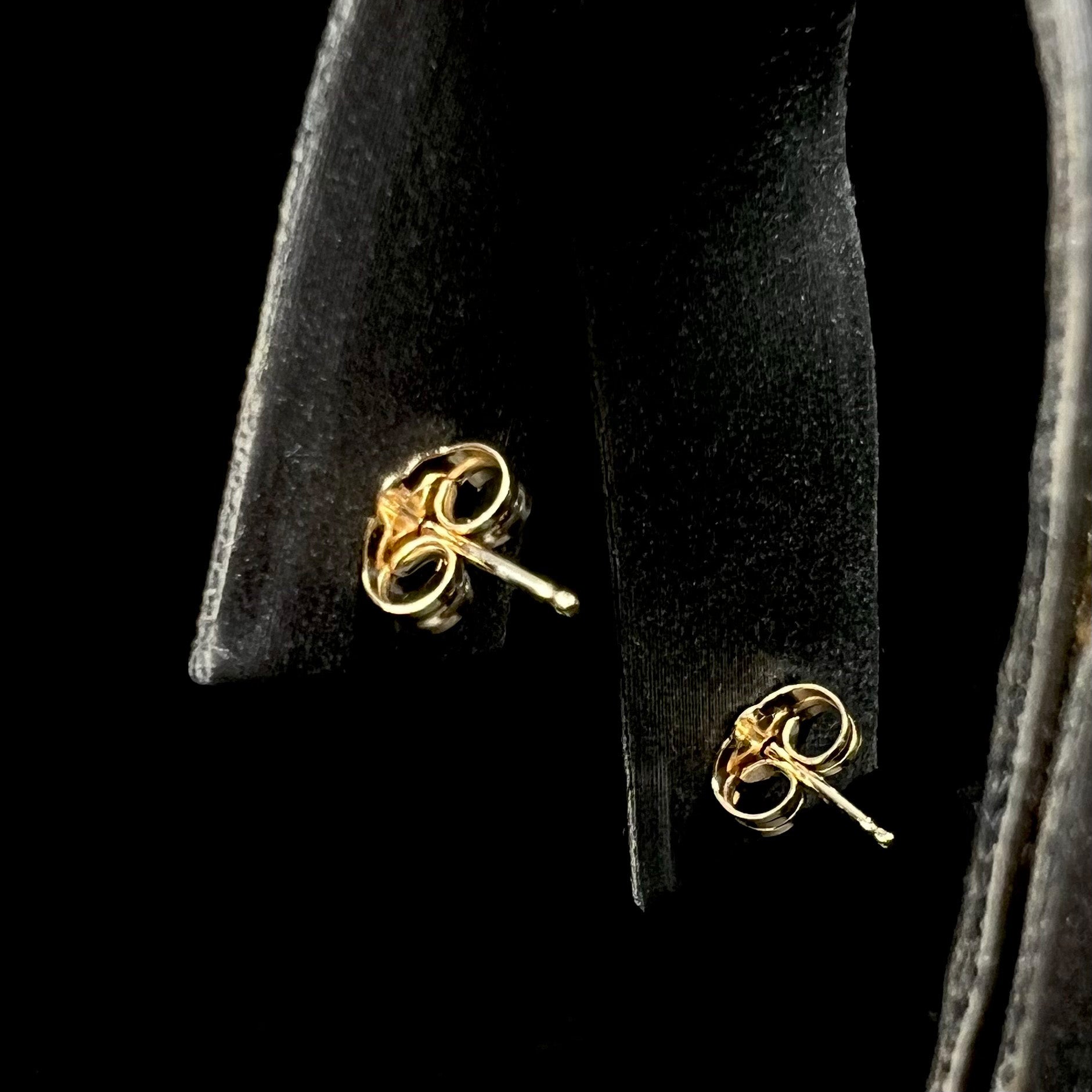 A pair of 14k yellow gold post earrings with butterfly backings, displayed on a black jewelry stand against a black background.