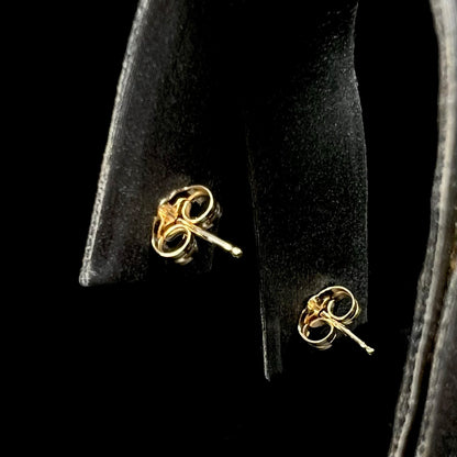A pair of 14k yellow gold post earrings with butterfly backings, displayed on a black jewelry stand against a black background.