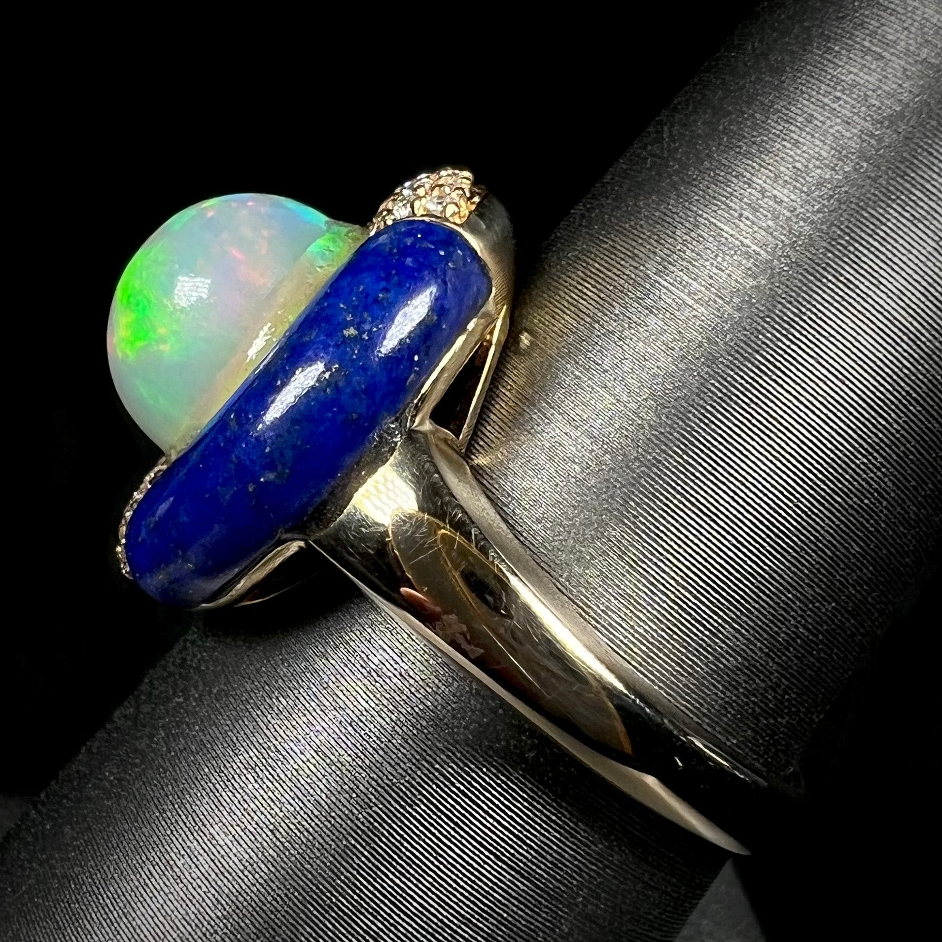 A lapis lazuli opal ring shown from the side view close-up on a ring display.  The ring's 14k yellow gold shank and carved lapis halo are in focus.