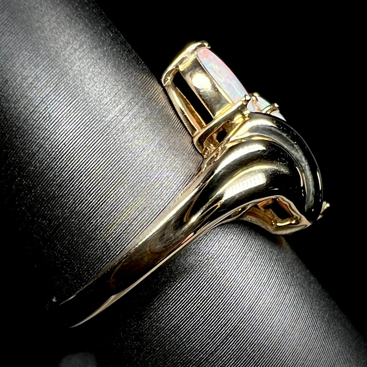 Side view of a 14k yellow gold Modernist-style opal ring on a ring display.
