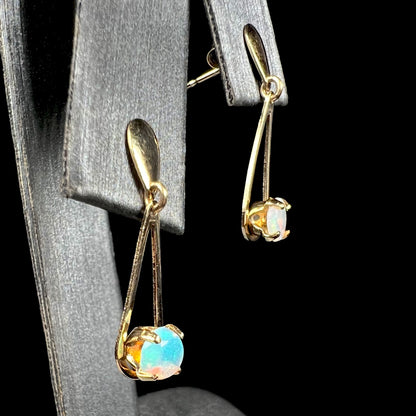 14k yellow gold opal dangle earrings shown from angle on earring display against black background.  Greenish blue opal is in focus.