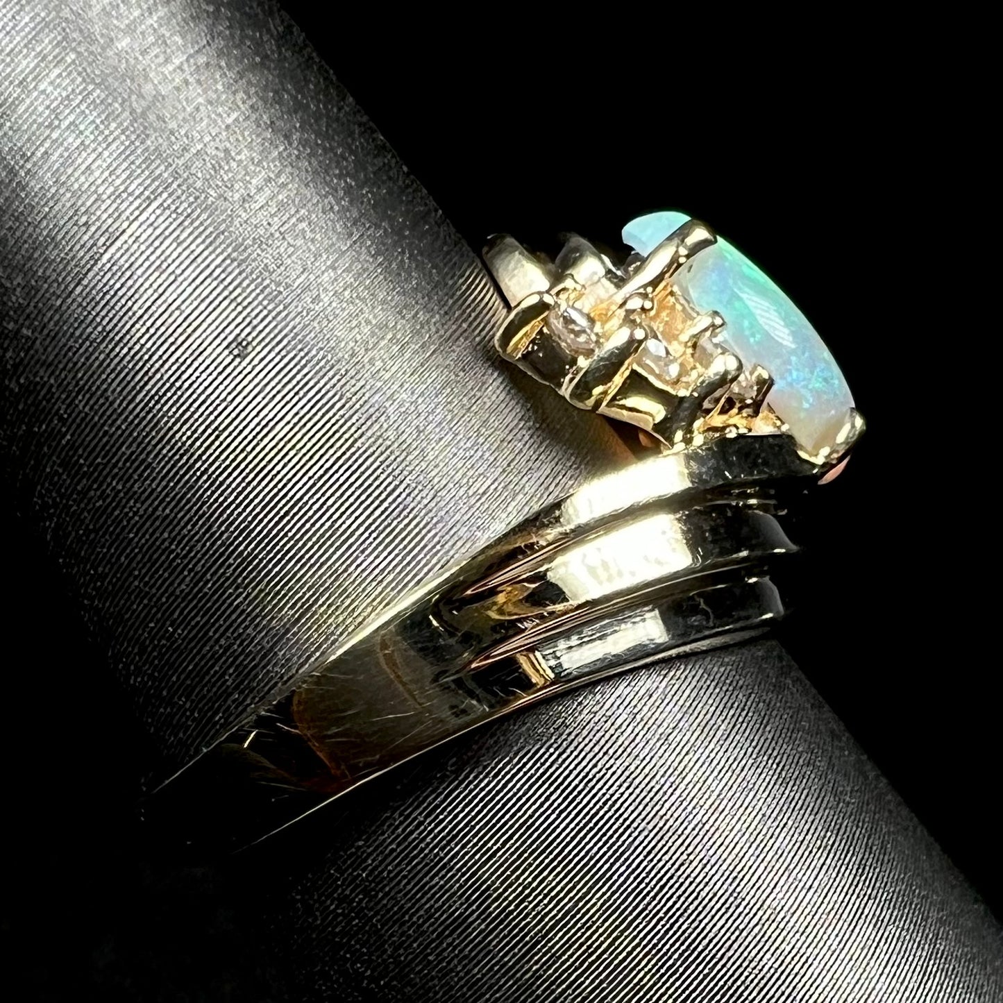 Side view of 14k yellow gold opal ring on ring display, focused on one side of ring's shank