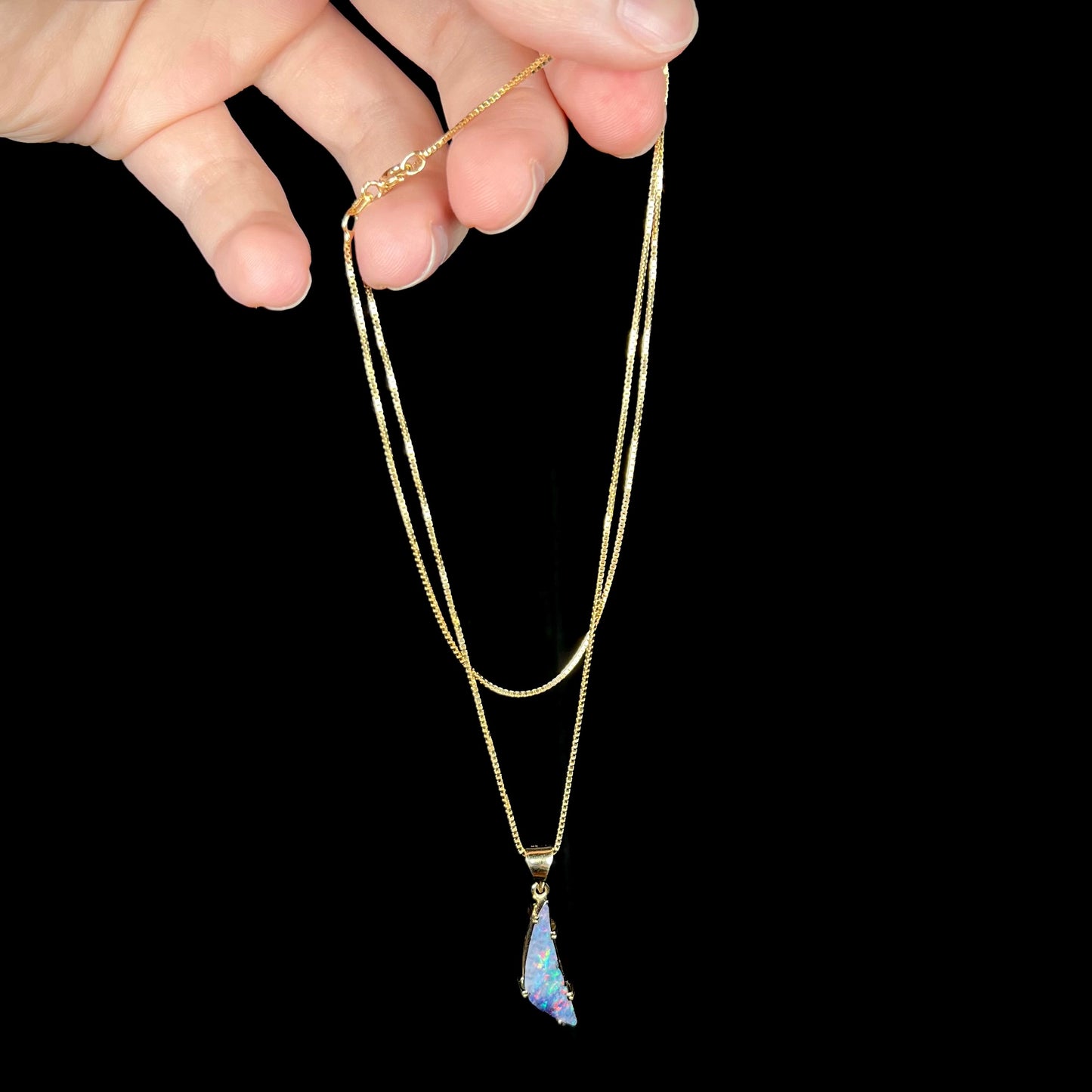 Hand dangling 18k Australian boulder opal necklace against black backdrop
