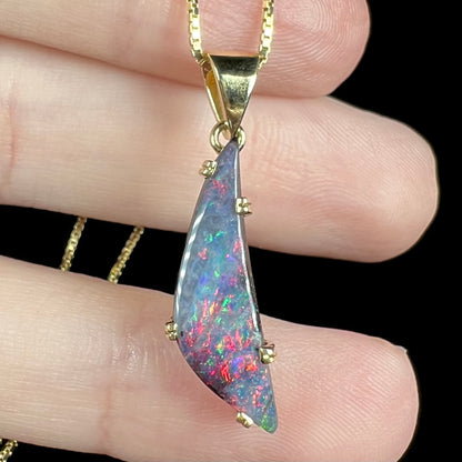 Close-up of 18k gold boulder opal pendant with red, pink, and green flashes, resting on fingers