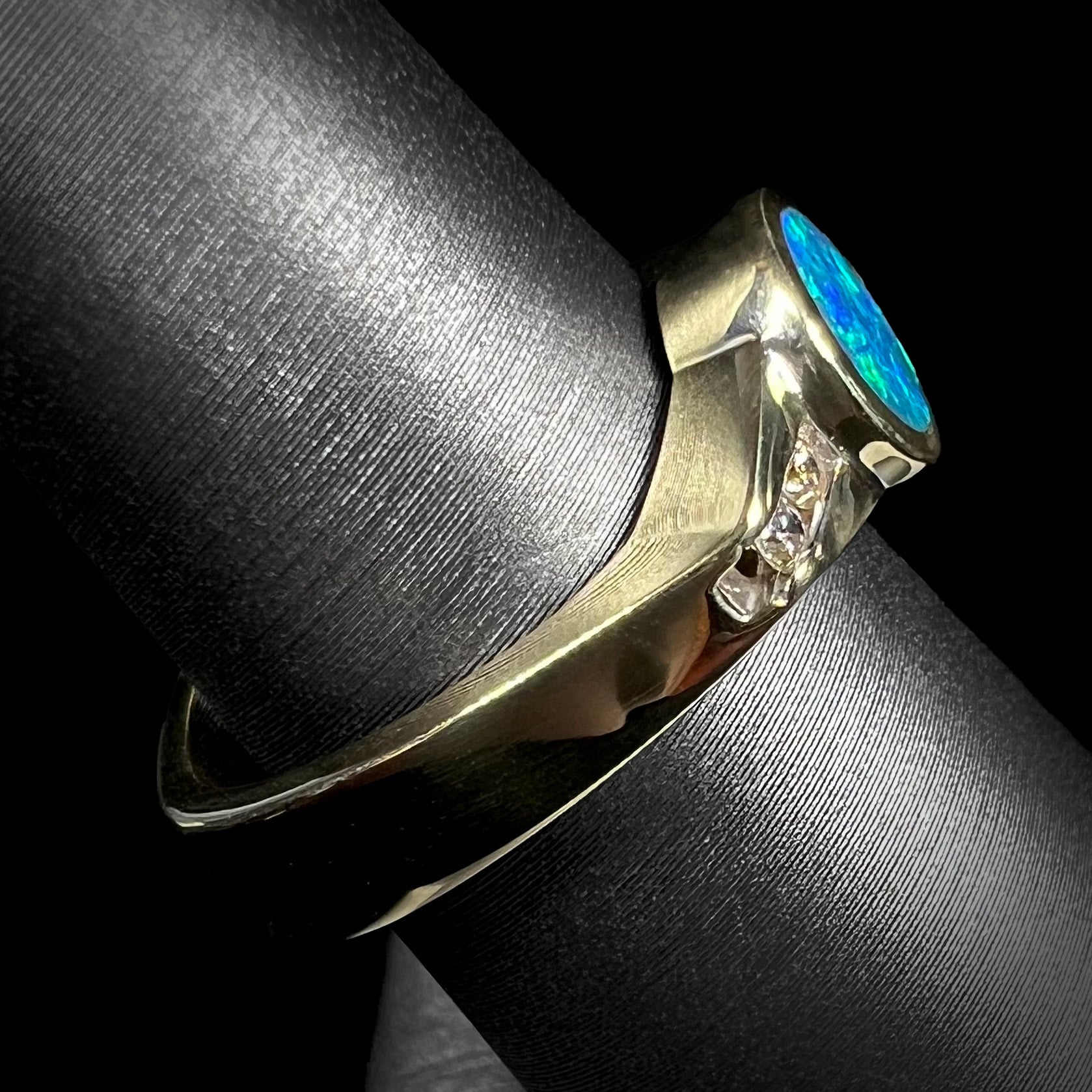 Side profile of a solid 18k gold square Euro shank opal ring, shown up close on a ring display.  Studio light shows deep blue opal color.