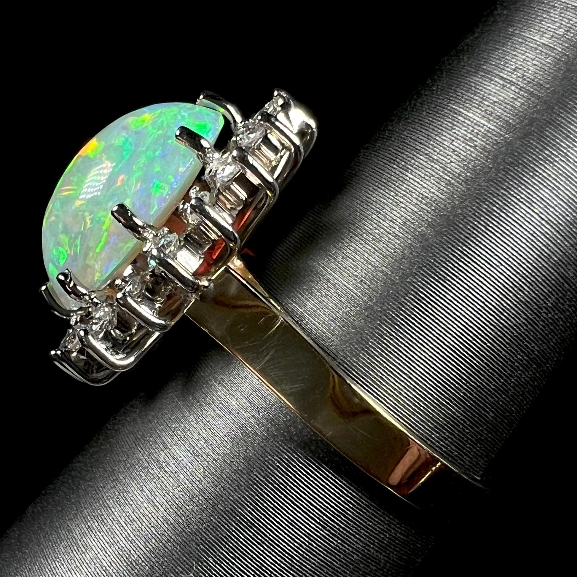 A side-angle view of a 4.30ct Lightning Ridge fire opal engagement ring in 18k gold.  The opal's green fire is visible, with the gold shank in focus.