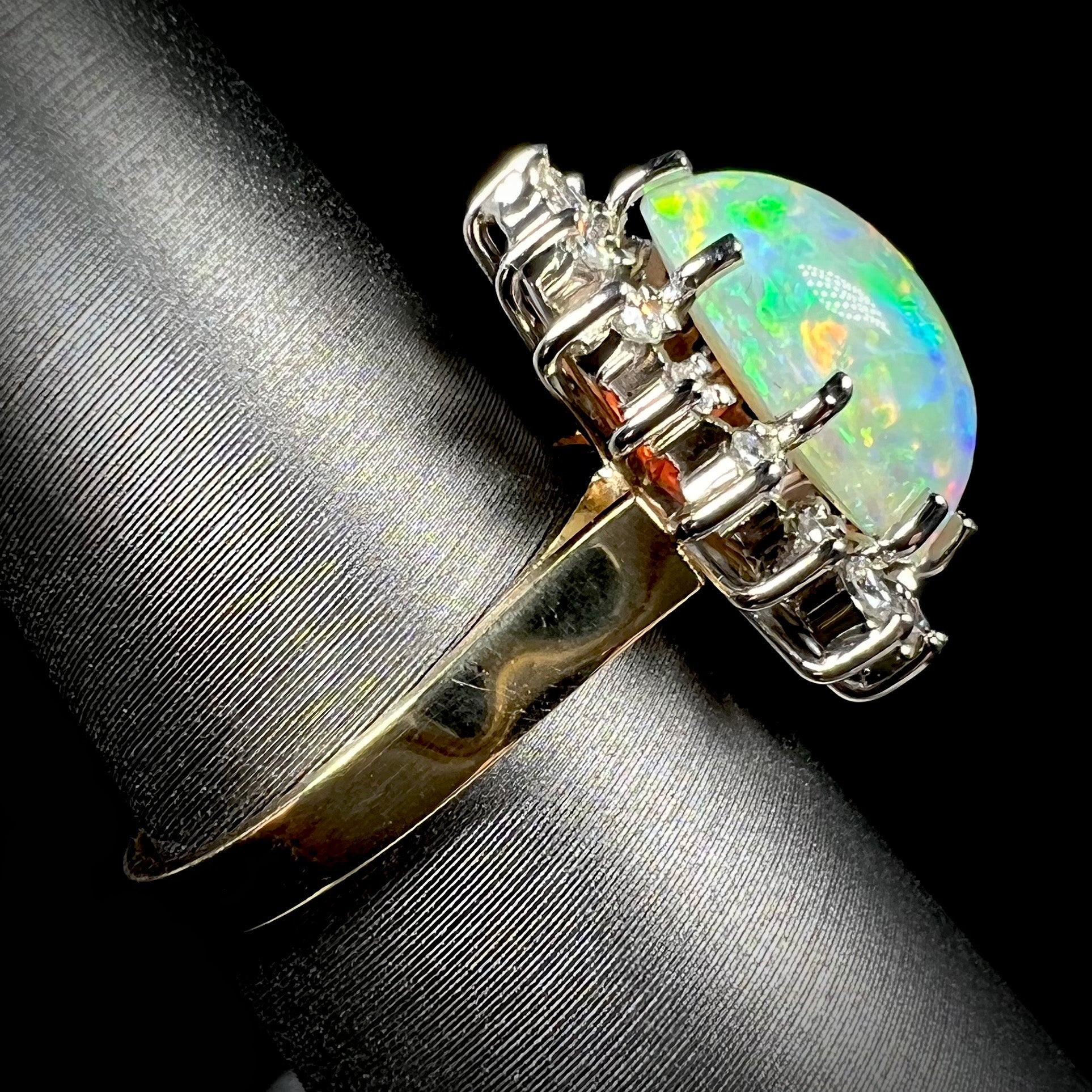 A side-angle view of a 4.30ct Lightning Ridge fire opal engagement ring in 18k gold.  The opal displays a bluish-green fire with red flashes.