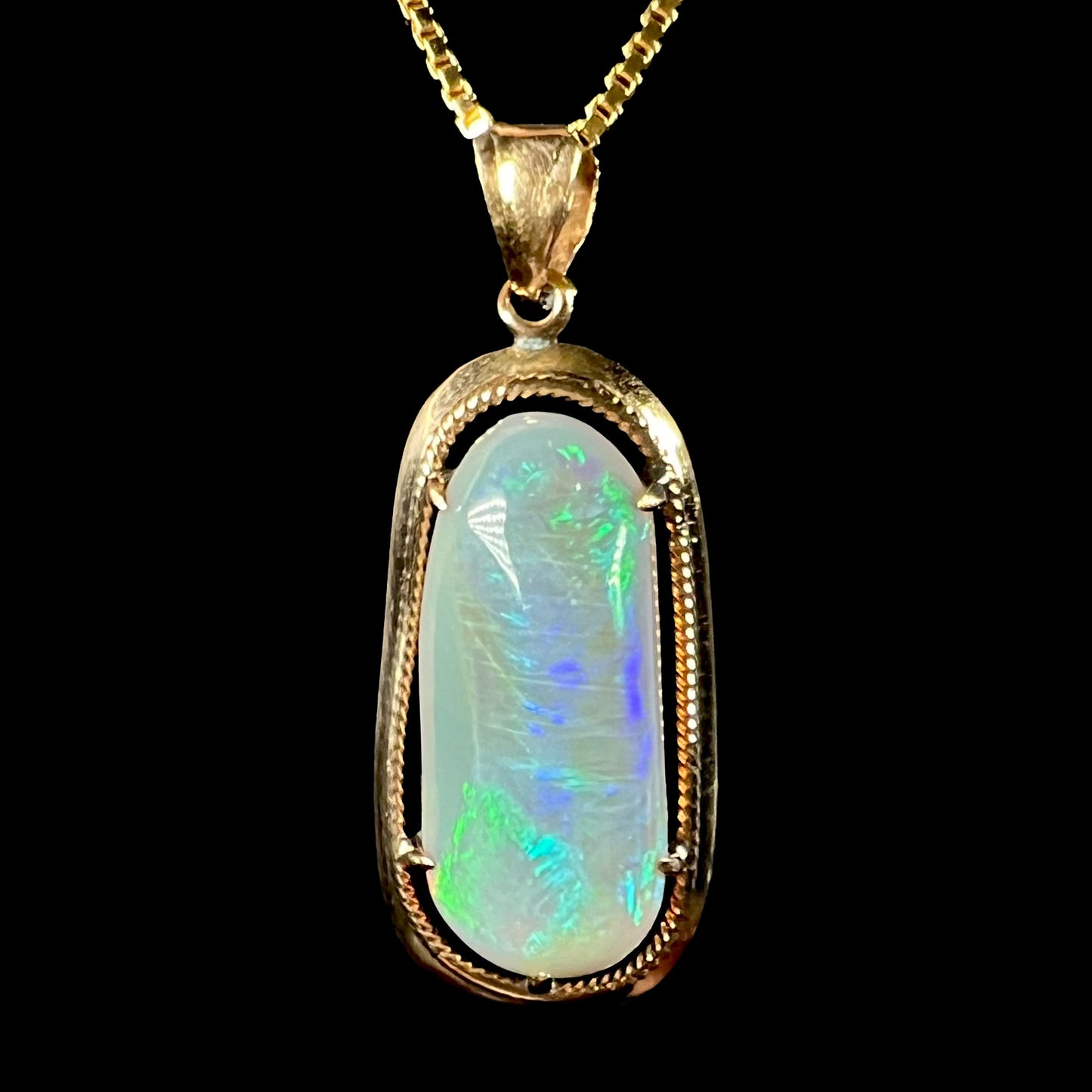 A macro view of an 18k gold Lightning Ridge opal pendant against a black background, showing green and blue flashes.