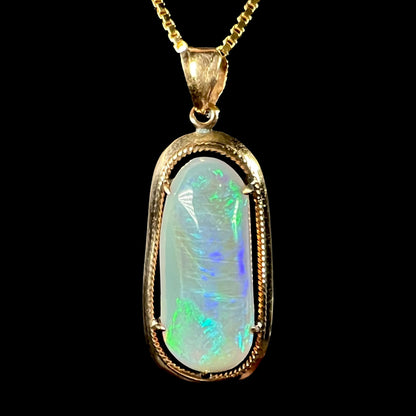 A macro view of an 18k gold Lightning Ridge opal pendant against a black background, showing green and blue flashes.