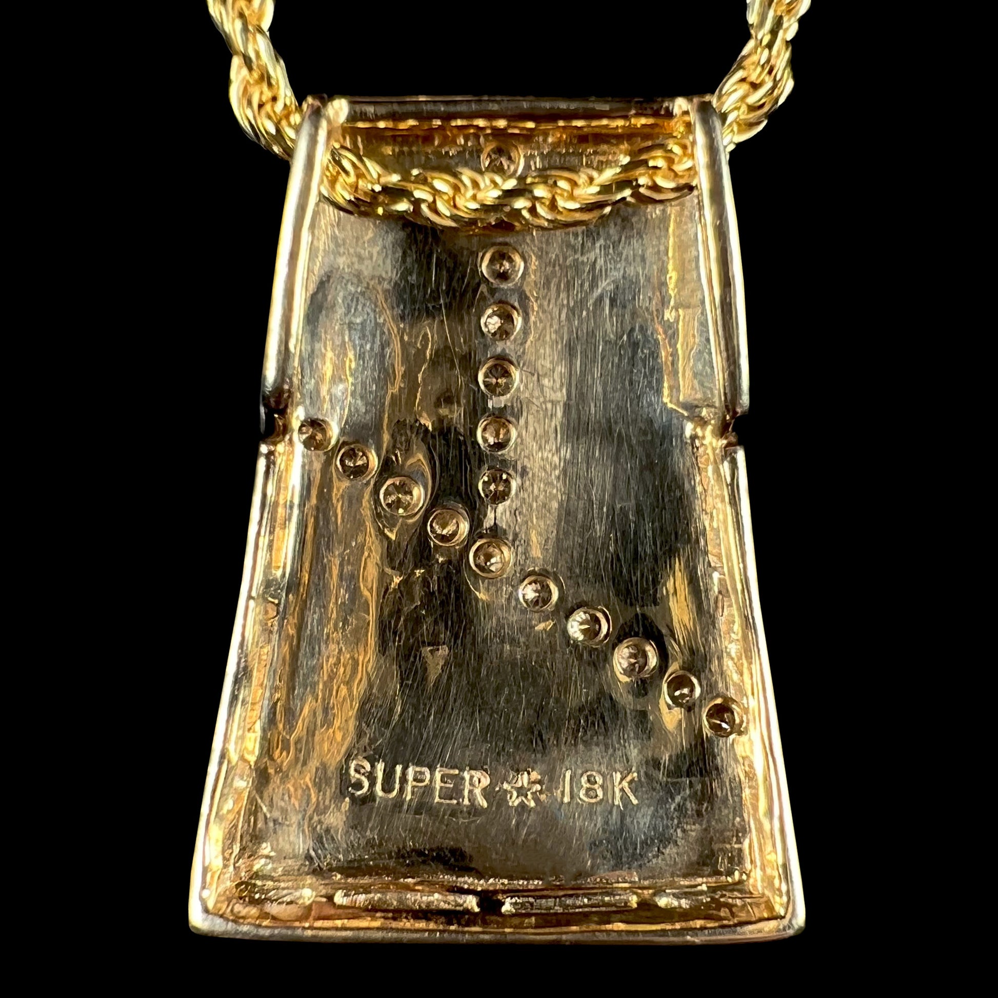 Back of an 18k yellow gold men's pendant, focusing on the hallmark stamps "SUPER", a star icon, and "18K".